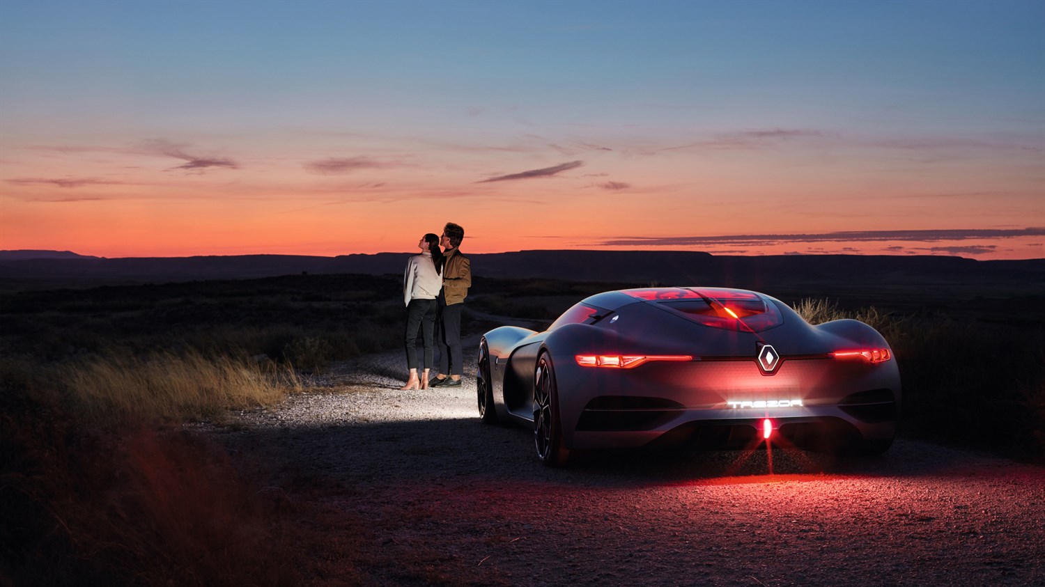 A couple standing ahead of the Renault TREZOR concept car are looking at the sky